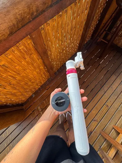 Mão segurando um bastão de selfie em um deck de madeira.