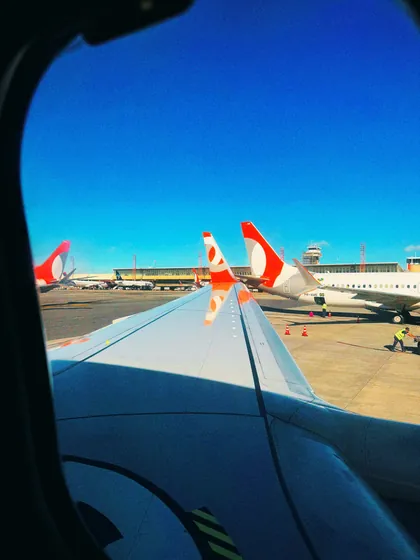 Vista da janela de um avião, com a asa e aeronaves na pista.